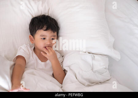3 ans peu malade ou maladie Asian boy à la maison sur le lit, triste enfant portant sur white lit avec oreiller et couverture, top view with copy space Banque D'Images