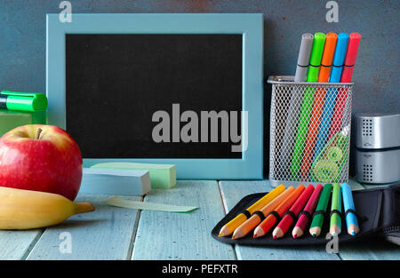 Papeterie, pomme et banane sur une table en bois en face du tableau noir avec l'espace de texte Banque D'Images