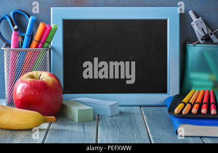 Papeterie, pomme et banane sur une table en bois en face du tableau noir avec l'espace de texte Banque D'Images