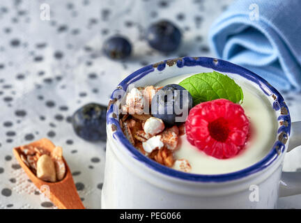 Yaourt au muesli, de framboise, de bleuet et de noix, dessert sain avec plus de fruits rouges sur fond boutonneuses de lumière Banque D'Images