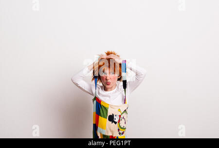 Une petite fille avec une perruque et un costume clown dans un studio, sticking out tongue. Banque D'Images