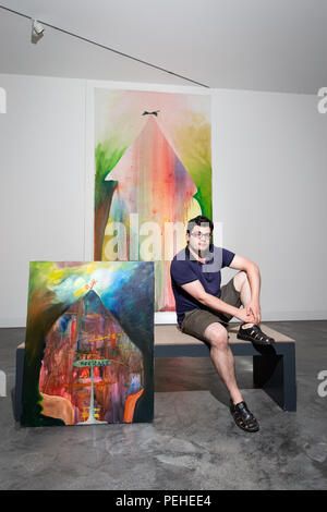 Osnabrück, Allemagne. 09Th Aug 2018. Artiste russe Yury Kharschenko s'assoit à côté de ses tableaux "Maison de sourire" (huile sur toile, 2016, à l'arrière) et "Maison du patrimoine" (huile sur toile, 2014) à la Felix-Nussbaum-Haus. Credit : Friso Gentsch/dpa/Alamy Live News Banque D'Images