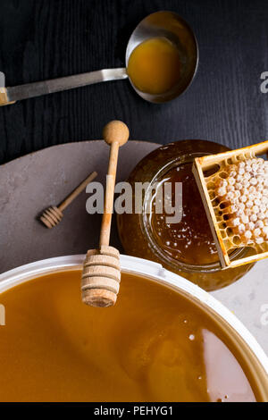 Le miel en pot et grand seau, honeycomb et bâton en bois, métal louche Banque D'Images