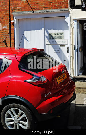 Une voiture rouge garée dans un garage ouverture montrant un 'No Parking sign' sur une propriété à long Melford, Suffolk, UK Banque D'Images