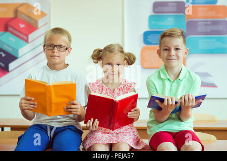 Trois écoliers lire des livres dans la salle de classe à l'école Banque D'Images