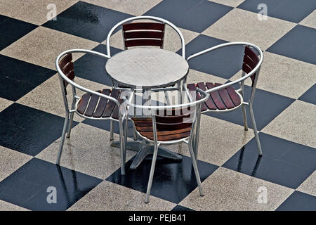 Une table et quatre chaises chrome siéger non utilisés sur un carrelage en damier. Banque D'Images