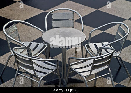 Une table et quatre chaises chrome siéger non utilisés sur un carrelage en damier. Banque D'Images