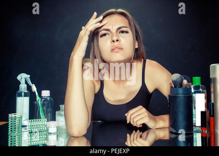 Insatisfait insatisfait de son auto en miroir sur fond de studio noir de la peau et l'acné. roblème concept. Matin, le maquillage et les émotions humaines concepts. Modèle caucasien au studio Banque D'Images