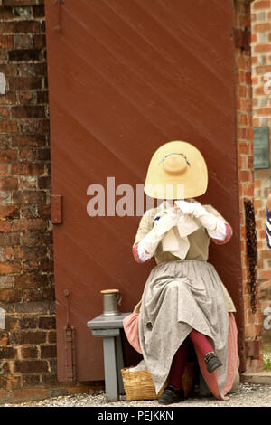 Reenactor femme dans la ville coloniale de Williamsburg, en Virginie. La broderie. Banque D'Images