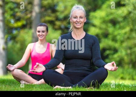 Ajustement mature femme sains d'âge moyen professeur de yoga yogi l'enseignement aux jeunes femmes à la pratique du yoga à l'extérieur dans un environnement verdoyant et tranquille naturel Banque D'Images