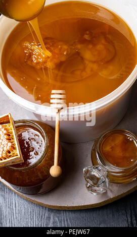 Le miel en pot et grand seau, honeycomb et bâton en bois, métal louche Banque D'Images