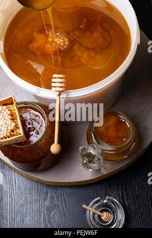 Le miel en pot et grand seau, honeycomb et bâton en bois, métal louche Banque D'Images