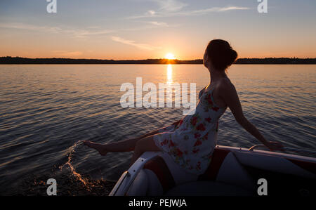 Jeune femme assise sur le bord d'un bateau sur un lac au coucher du soleil. Banque D'Images