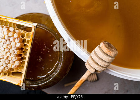 Le miel en pot et grand seau, honeycomb et bâton en bois Banque D'Images