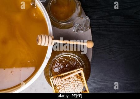 Le miel en pot et grand seau, honeycomb et bâton en bois Banque D'Images