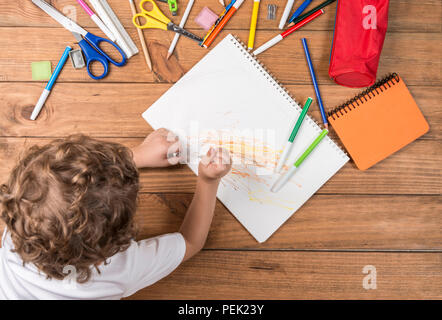 Concept de retour à l'école. Enfant couché sur les planches de bois et entouré par des fournitures scolaires griffonner sur un ordinateur portable. Banque D'Images