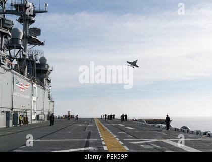 Un FA-18 E/F Super Hornet, un chasseur multirôle bimoteur capable de transporter des avions propulsé par des turboréacteurs General Electric F414-GE-400, survole le navire d'assaut amphibie USS Makin Island (LHD 8) lors d'essais en mer dans l'océan Pacifique le 9 décembre 2015. Le navire de la classe Wasp termine une disponibilité de maintenance progressive à San Diego. Le Super Hornet dispose d'une queue double, d'une avionique avancée et d'une sonde de ravitaillement pour les opérations en vol, démontrant l'intégration avec les opérations navales et les exercices d'aviation à bord des navires. Banque D'Images