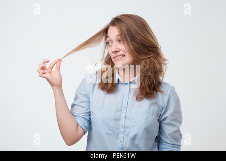 Portrait de jeune femme frustrée avec les pointes fourchues de cheveux sur fond blanc. Elle n'aime pas l'état de ses cheveux et elle pense à Banque D'Images