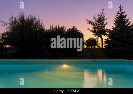 Piscine en plein air piscine liner bleu avec l'éclairage au crépuscule crépuscule coucher du soleil sur une bonne soirée de l'été, en France. Banque D'Images