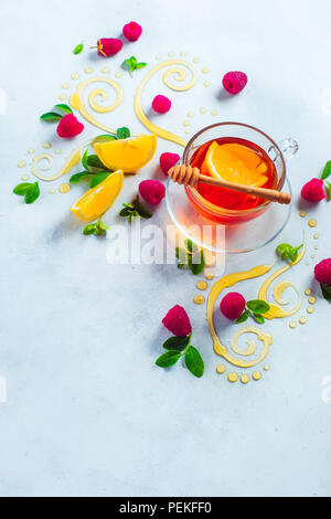 Thé au miel à partir de ci-dessus. Tourbillons au miel décoratifs, les tranches de citron, les baies et le thé dans une tasse en verre sur un fond en bois blanc, avec l'exemplaire de l'espace. Cuisine créative mise à plat Banque D'Images