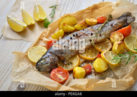 Truites au citron cuit au four avec des pommes de terre au romarin et tomates, servi sur du papier sulfurisé Banque D'Images