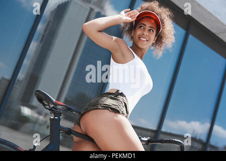 Jeune femme portant visière tennis style libre sur la rue équitation vélo près de toucher la fenêtre Retour à la hat smiling heureux Vue de dessous Banque D'Images