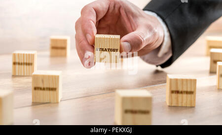 Businessman Hand Holding conceptuel cube de bois avec texte de la Stratégie sur le dessus de la table avec d'autres blocs. Banque D'Images