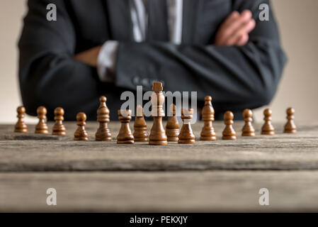 Costume homme assis les bras croisés en face de pièces des échecs à table . Banque D'Images