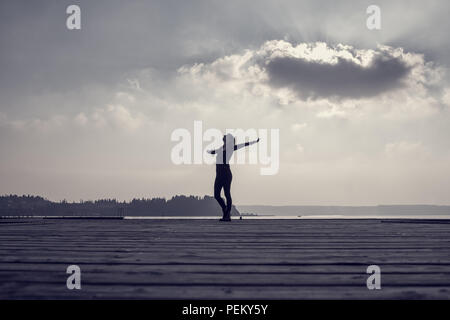 Tons rétro image d'une femme répandre armes contre sky comme elle se tient sur la jetée en bois. Banque D'Images