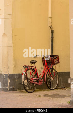 Un vélo rouge avec un panier s'appuie contre un mur Banque D'Images