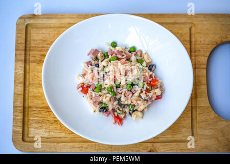 Salade de riz italien ou le riz froid dans une assiette blanche sur une planche avec fond blanc trouble. Banque D'Images