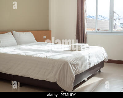 Chambre propre blanc dans l'hôtel, oreillers et serviettes sur le lit, les rideaux et la lumière de la fenêtre de l'extérieur avec vue sur la campagne environnante. dans les maisons Banque D'Images