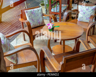 Fauteuils en bois avec coussins, table ronde en bois avec fleur en pot sur table et étagère en bois sur planche en bois marbre dans le café. Banque D'Images
