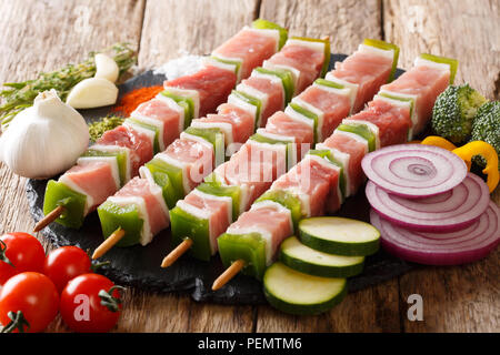 Barbecue pour matières shish kebab avec du poivre et le lard sur les brochettes, close-up et les ingrédients, légumes, épices, fines herbes sur la table horizontale. Banque D'Images