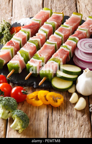 Shish kebab de porc cru avec du poivre sur les brochettes, close-up et d'ingrédients, des légumes, des herbes sur la table verticale. Banque D'Images