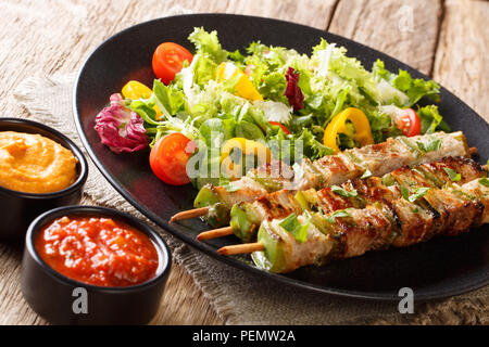 Porc barbecue avec du poivre en brochettes avec une salade fraîche sur une plaque noire et le ketchup et la moutarde gros plan sur la table horizontale. Banque D'Images