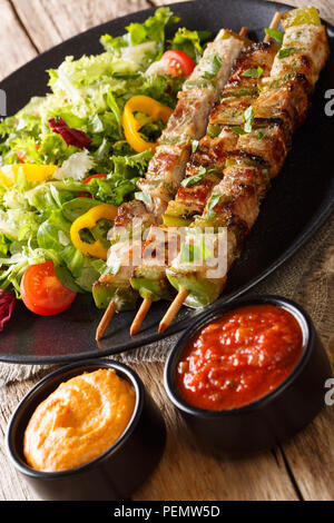 Délicieux kebab en brochettes avec une salade de légumes frais sur une assiette et la sauce sur la table verticale. Banque D'Images