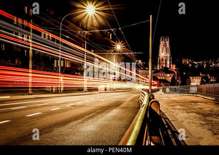 Une longue exposition photo de nuit de Fribourg en Suisse, avec des sentiers de véhicule léger rouge à gauche et la cathédrale Saint-Nicolas sur l'arrière-plan Banque D'Images