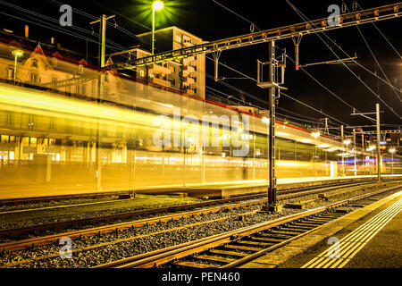 Une longue exposition shot d'un train entrant dans la gare de Fribourg, en Suisse, avec des sentiers de lumière colorée sur le côté et la ville en arrière-plan Banque D'Images