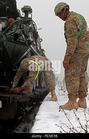 Le Sgt. Ryan Powell (à droite) surveille la CPS. Tyler Minnick (à gauche), les deux troupes fantassin affecté à K, 3e Escadron, 2e régiment de cavalerie, comme Minnick supprime une cale d'un véhicule de combat blindé Stryker pendant les opérations de tête, 11 janvier, à Konotop, Pologne. Avant de véhicules peuvent être déplacé de le train, les soldats doivent effectuer les procédures de démarrage à froid et retirer les équipements utilisés pour maintenir les véhicules en place. (U.S. Photo de l'armée par le Sgt. Paige Behringer, 10e Appuyez sur Camp de siège) Banque D'Images