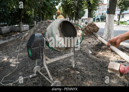 Travailleur de la construction Ajouter les ingrédients pour le mélange à la bétonnière sur chantier à l'aide d'une pelle pendant les travaux de construction de trottoirs Banque D'Images