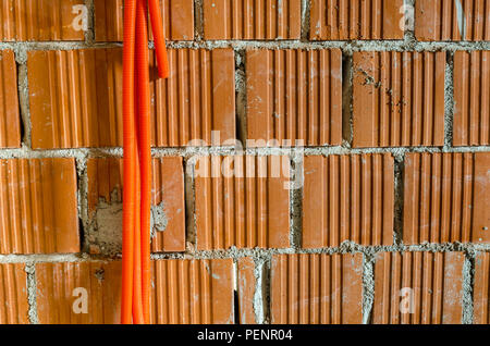 Tuyaux en plastique orange pour câble électrique accrochée à un mur de briques d'une chambre dans une maison en construction. Banque D'Images