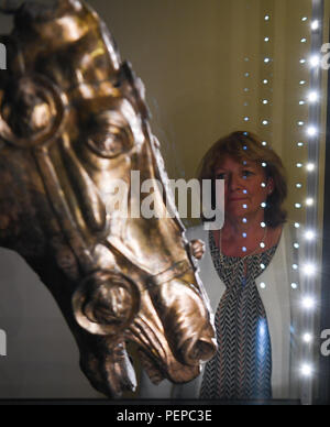 Bad Homburg, Allemagne. Août 17, 2018. Restaurateur Angelika Ulbrich se penche sur les quelque 2000 ans tête de cheval antique de Waldgirmes, qui est exposé dans une vitrine dans le fort romain Saalburg près de Bad Homburg. La tête de cheval en bronze doré a été trouvé lors de fouilles archéologiques dans Lahnau-Walgirmes dans le centre de Hesse en 2009 et a été entièrement restauré. La précieuse sculpture a été l'objet de plusieurs années de procès. (Dpa "Roman sur la tête de cheval à Saalburg voir' à partir de 17.08.2018) Crédit : Arne Dedert/dpa/Alamy Live News Banque D'Images