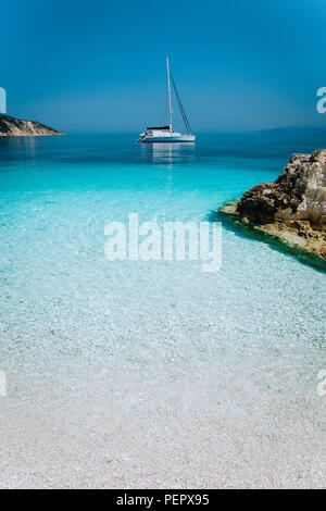 Lagon bleu azur avec catamaran à voile bateau au mouillage. Plage de galets blanc pur, quelques rochers dans la mer Banque D'Images