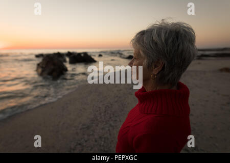 Senior woman standing on beach pendant le coucher du soleil Banque D'Images