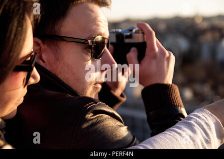 Couple apprécie le soleil sur le toit et un jeune homme photographier Panorama de la ville. Couple taking pictures of le coucher du soleil sur le toit. Banque D'Images