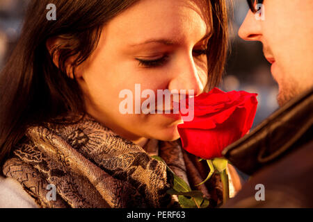 De joie et d'amour du couple pour la Saint-Valentin. Couple aimant profiter du soleil sur le toit et belle fille sent une rose rouge, symbole de l'amour. Banque D'Images