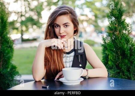 Portrait of beautiful smiling young white middle eastern woman femme aux cheveux longs assis à table, à huis clos. Femme avec tasse de co Banque D'Images