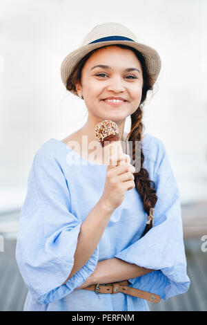 Portrait of beautiful happy smiling laughing Caucasian blanche fille brune femme avec la peau tannée en robe bleue et hat eating ice-cream cone, coucher du soleil Banque D'Images