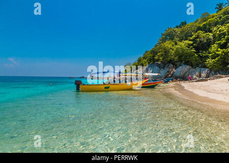 Des bateaux de tourisme colorés ancrée dans les eaux peu profondes de l'éblouissante plage de Rawa ; son sable blanc poudreux, forêt luxuriante et de gros rochers en arrière-plan... Banque D'Images